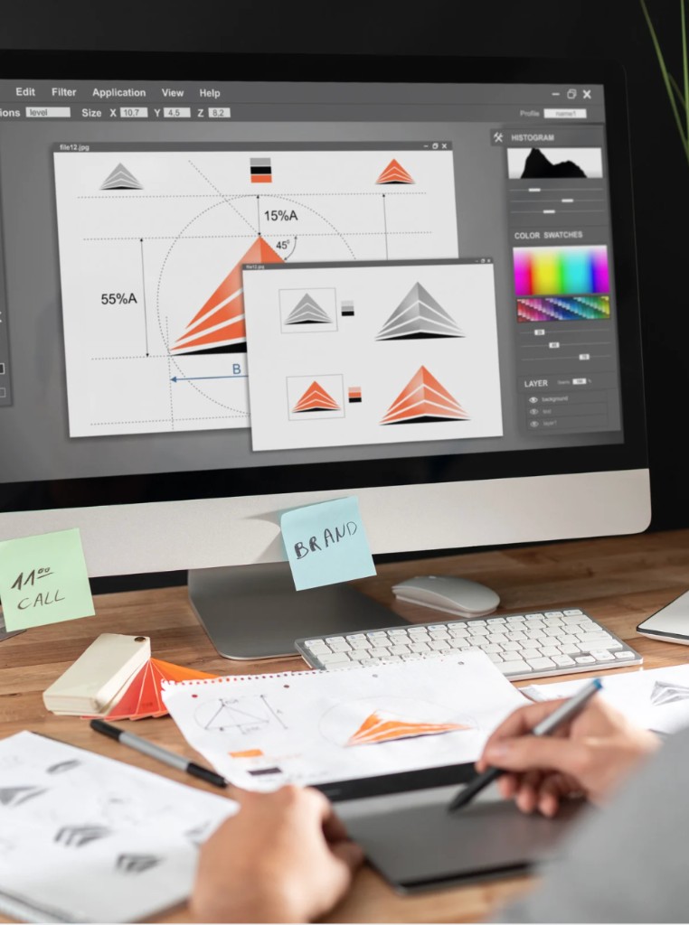 Designer developing logo concepts on screen with sketches and color swatches on the desk
